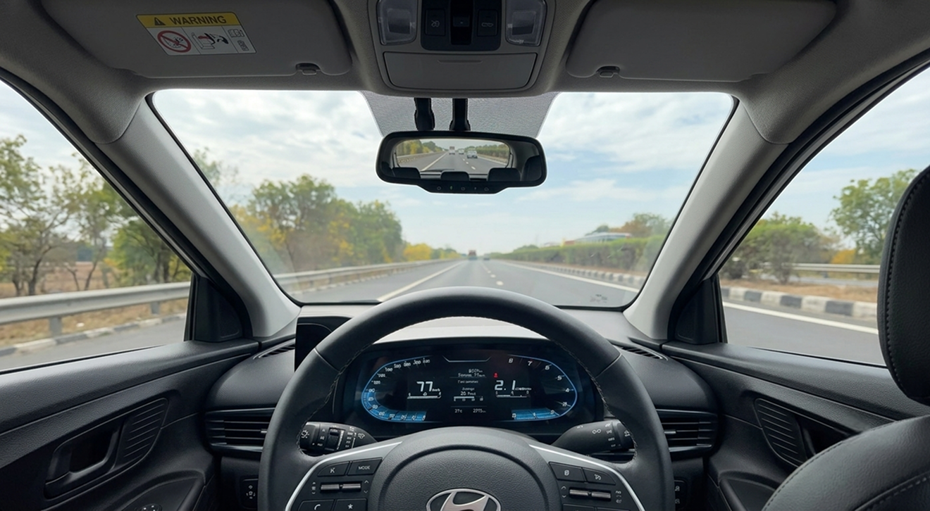 Driver's point of view from inside a car driving on a highway, showing the steering wheel and digital instrument panel